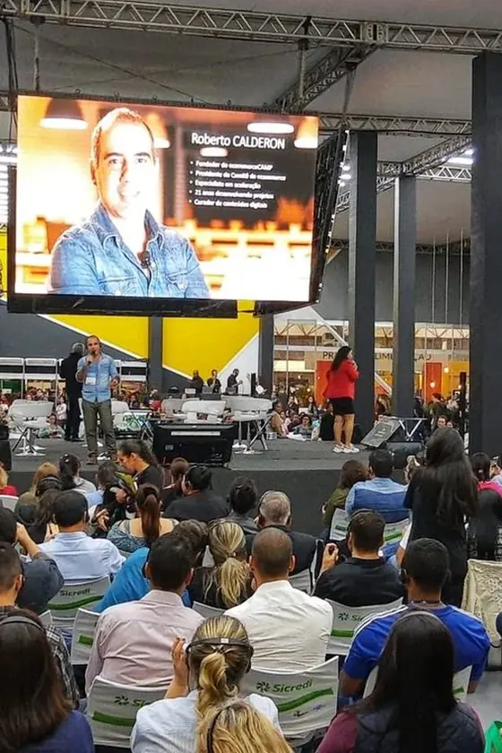 Roberto Calderon no palco principal, com o telão atrás e a plateia lotada